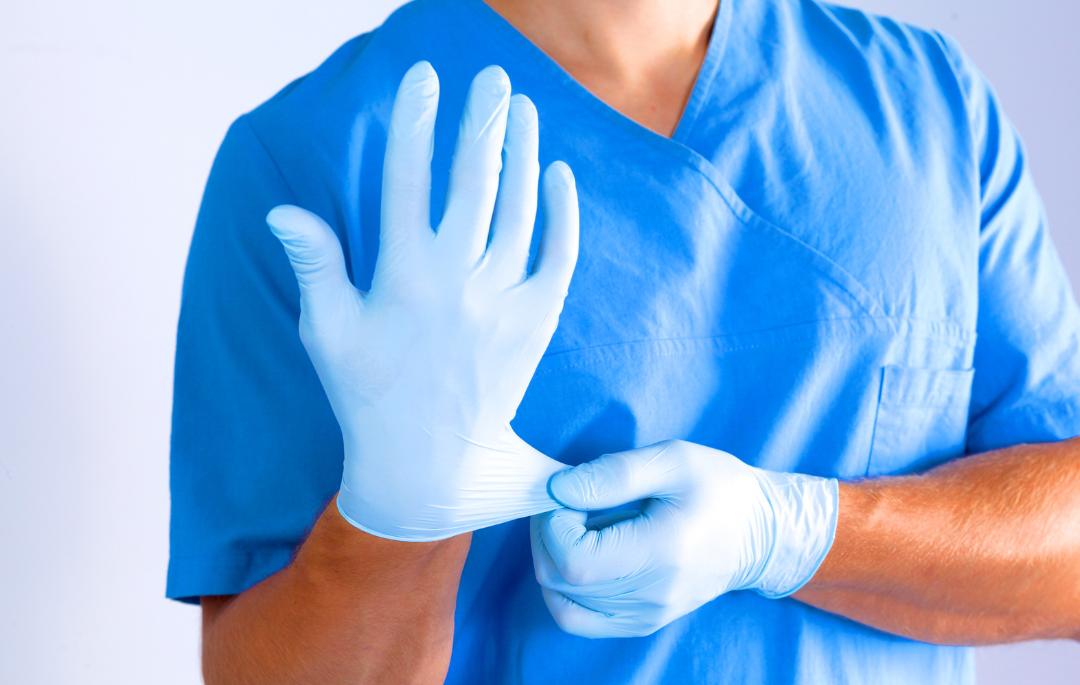 Diferencia entre los guantes de látex y nitrilo: ventajas, desventajas y usos profesionales Profesional sanitario ajustándose guantes desechables, ilustrando la diferencia entre los guantes de látex y nitrilo en el ámbito médico.
